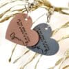 Image shows two leather heart keychains on gold leaves.