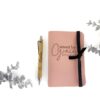 Image shows a pink leather journal and personalized pen with some sparkly silver leaves